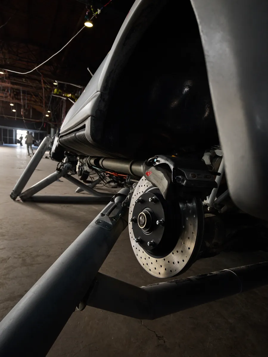 A car raised on a two-post lift, seen from underneath with the brake disc and suspension arms in the foreground